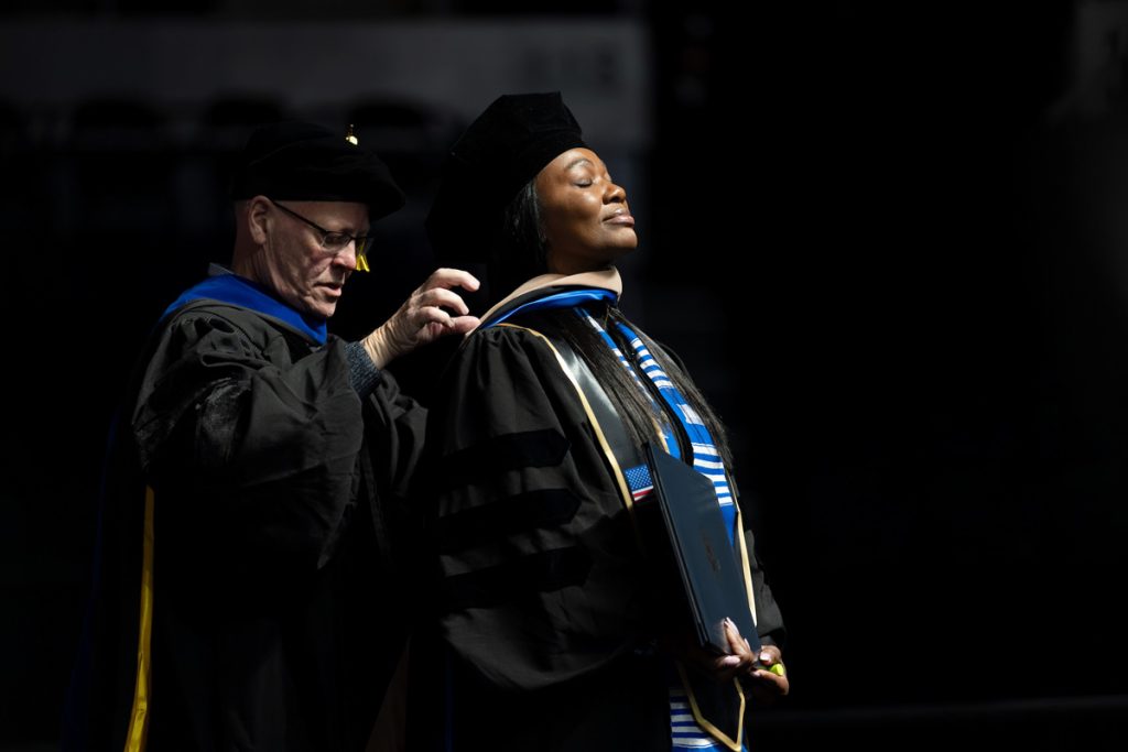 Male JWU faculty member placing a doctoral hood over the female graduate's head during the commencement ceremony.