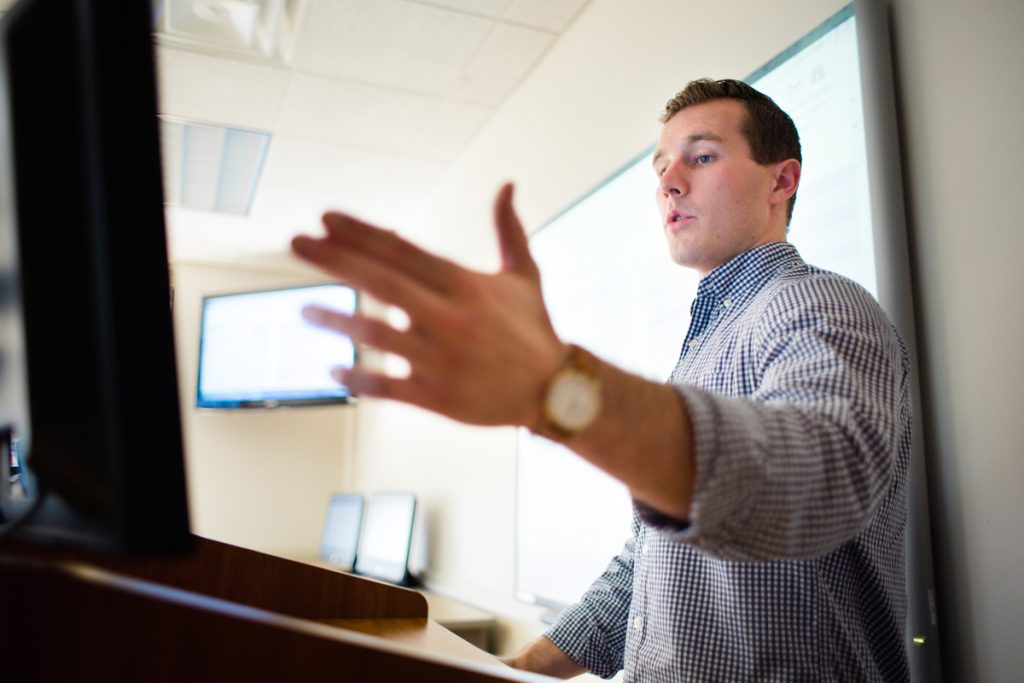 Male professor in front of classroom gesturing with arm extended.