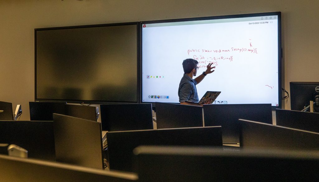 Male student silhouetted as he stands in front of a projection screen on which data is displayed.