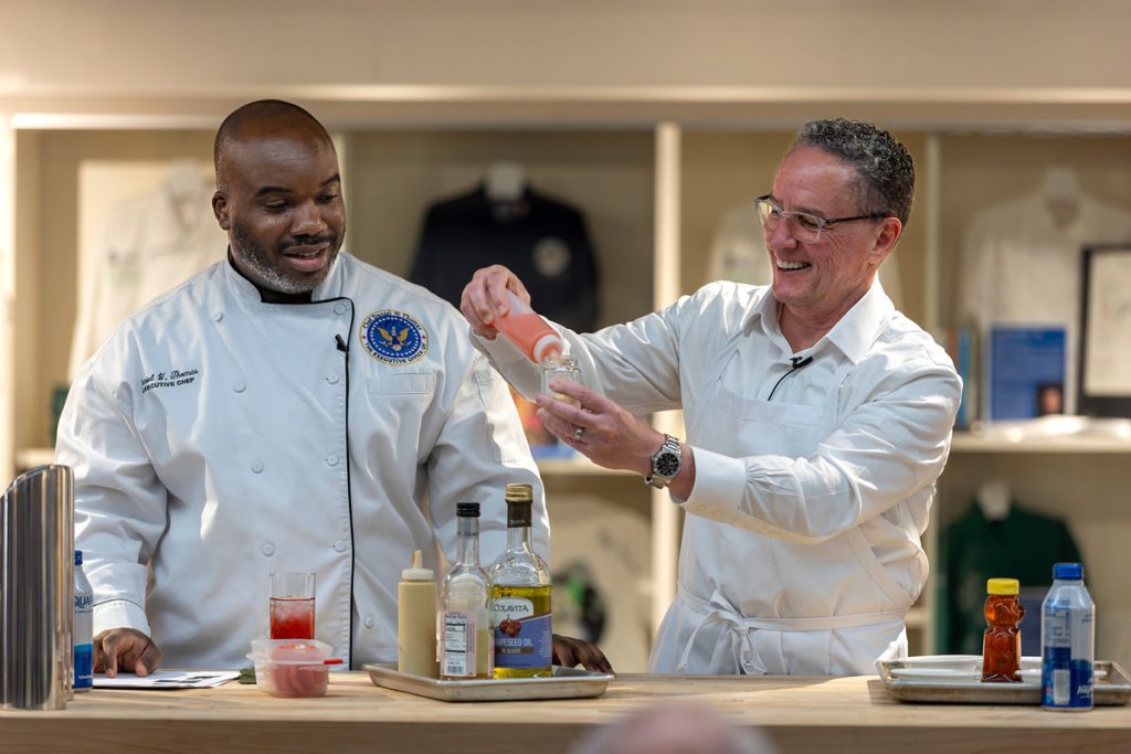 Celebrity Chef Daniel Thomas in his chef's whites uniform preparing a condiment with JWU Providence President Joe Greene.