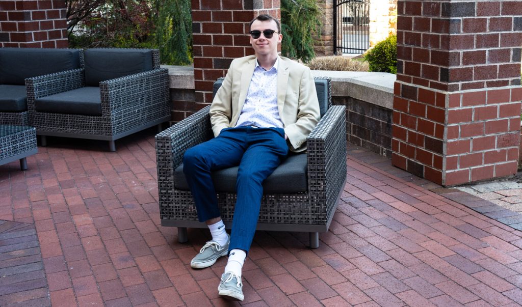 Power wearing business casual clothing and sunglasses, sitting in a chair on the brick paved outdoor patio with brick columns behind him at the Marriott Quincy.