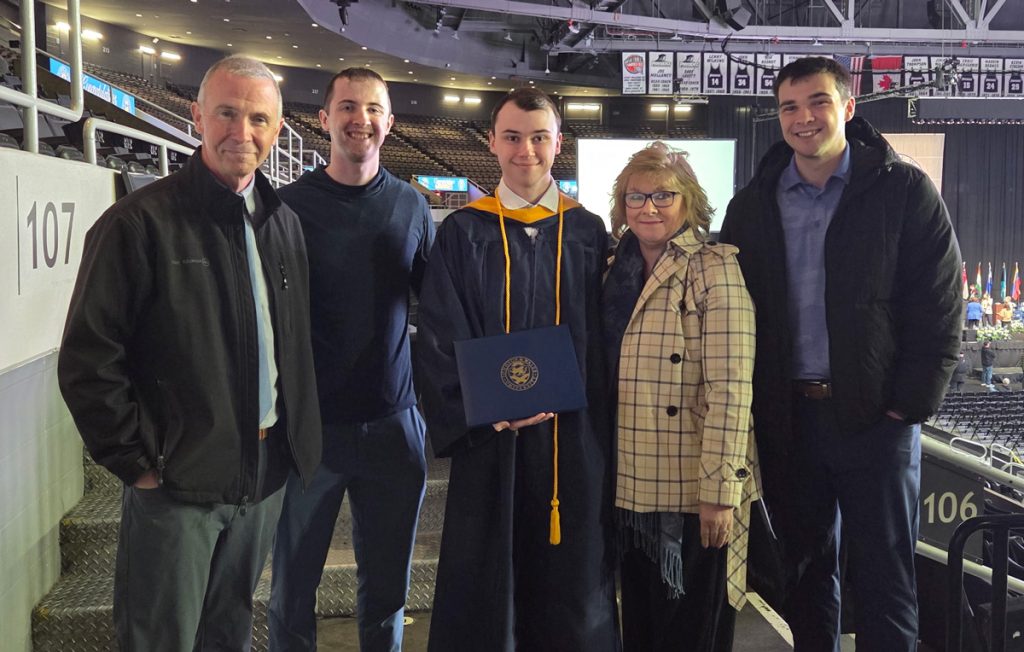 Tyler Power holds his JWU diploma, while standing in the Amica Pavilion with his mom, dad and two other male family members