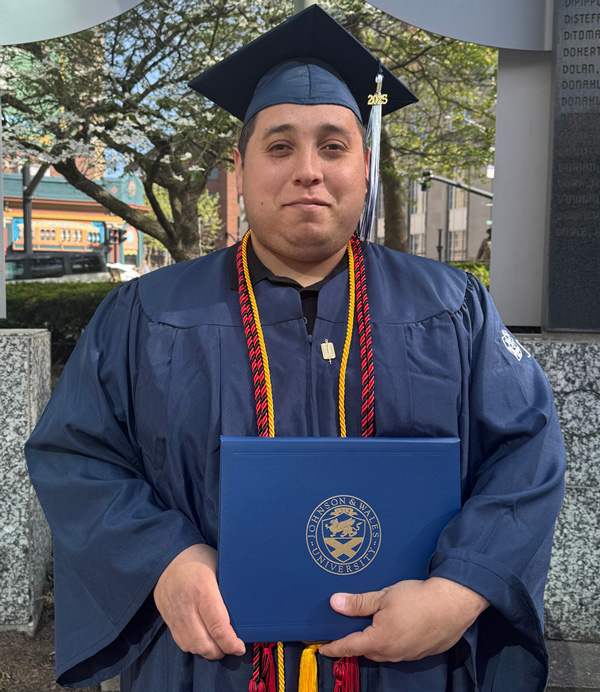 Albert Torres in cap and gown, holding his diploma.