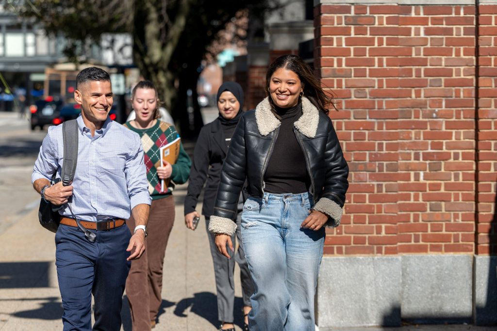 A male and three female JWU students walk together on a street bordering the Providence Downcity campus.