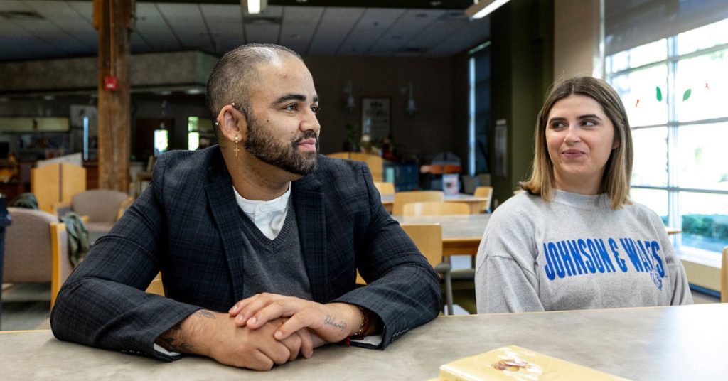 Photo of Amado Amesquita-Santos seated next to fellow student, McKenzie Thibeault, in the JWU library in the Friedman Center on the Harborside Campus in Providence, Rhode Island. 