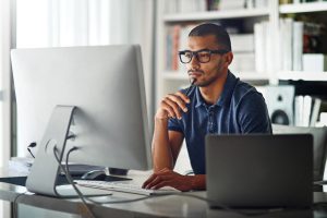 man sitting at desk thinking while looking at computer