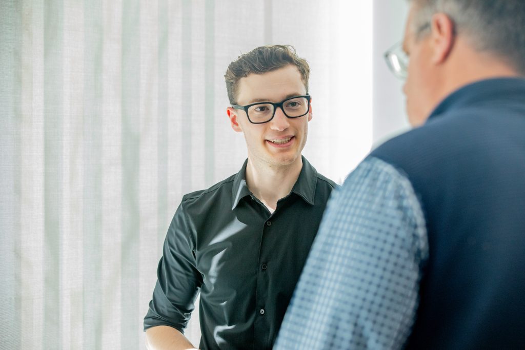 Young male student at a JWU Symposium talking to a male individual off camera.