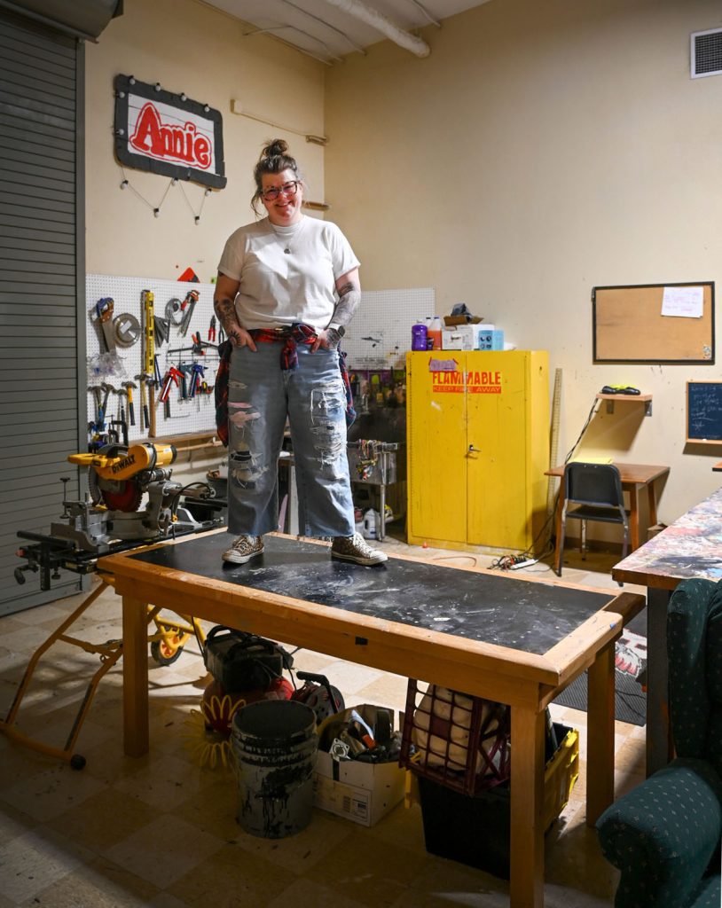 Mikala Schimke stands on a table in the prop room at the theatre where she worked in the production of the play, Annie.