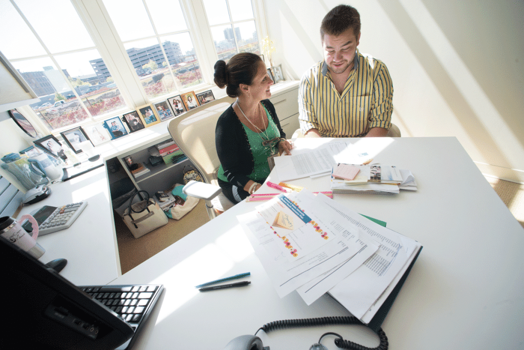 A female instructor seated at a table with a young male student, looking at an array of marketing materials.